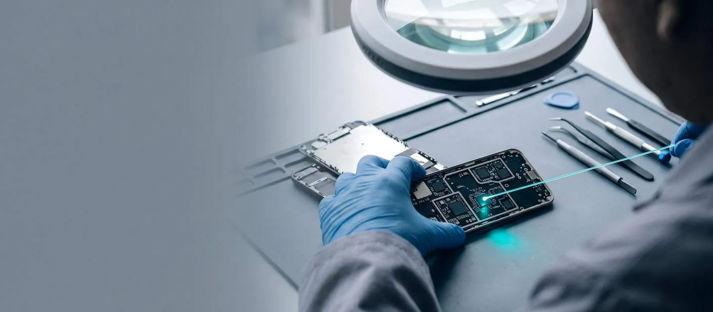 Técnico con guantes revisa la placa de un teléfono bajo una lupa de laboratorio